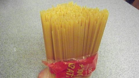 Spaghettipackung öffnen: Die Methode wirkt ein wenig cool, ist aber in Wahrheit einfach einfach. Die Hand hält eine Packung Spaghetti, während sie geöffnet wird, auf einer grauen Tischoberfläche.