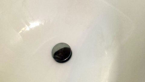 Ein Abflussstopfen liegt im Becken, während unansehnliche Wasserrückstände auf den weißen Wänden sichtbar sind. Schlechte Gerüche entstehen leicht.