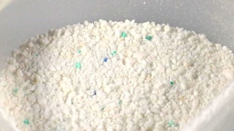 Weißes Waschpulver in einer transparenten Schüssel, bereit zur Anwendung im Putzmittelprozess zum Reinigen von Kleidung.
