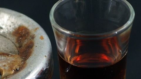 Ein Glas mit dunkler Flüssigkeit steht neben einem rostigen Metallobjekt, das Essig enthält, um Rost zu entfernen.