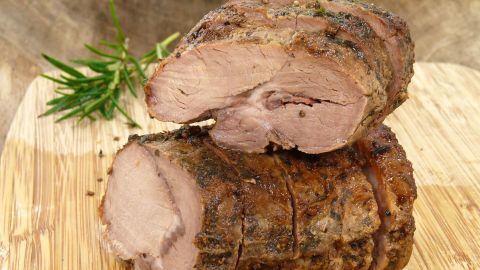 Saftiger Sonntagsbraten in Scheiben auf einem Holzbrett, umgeben von frischen Kräutern und rustikalem Ambiente.