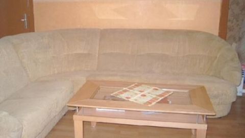 Ein beigefarbenes Sofa steht vor einer zweifarbig gestrichenen Wand, ein Tisch mit Decke davor, in einem gemütlichen Wohnzimmer.