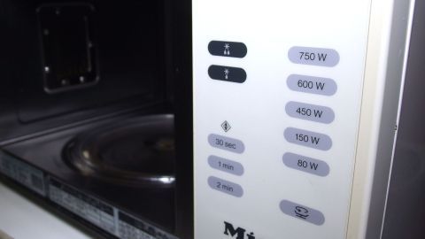 In einer Mikrowelle leuchtet das Bedienfeld und zeigt verschiedene Leistungsstufen an, während die Innenraumtemperatur steigt.
