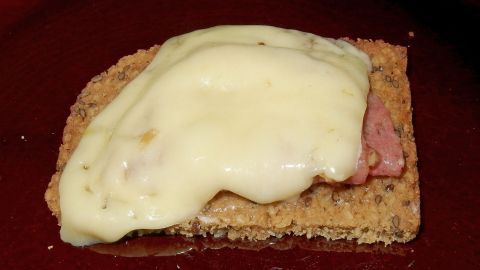 Eine Scheibe Brot liegt auf einem Teller, belegt mit Schinken und geschmolzenem Käse, ideal für ein leckeres Snack.