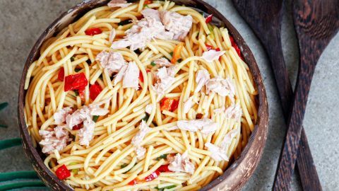 Ein Salat aus Spaghetti mit Thunfisch und Paprika liegt in einer Holzschüssel auf einem grauen Tisch, bereit zum Servieren.