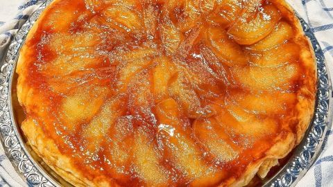 Eine goldbraune Apfel-Tarte liegt auf einem silbernen Teller, umgeben von einem karierten Tuch, und glänzt verlockend.