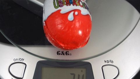 Ein Kinderüberraschungsei liegt auf einer digitalen Waage, die 34 Gramm anzeigt, in einer neutralen Umgebung.