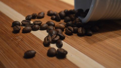 Kaffeebohnen fallen aus einer Tasse auf ein Holzbrett, ideal für die Zubereitung von gutem italienischen Kaffee.