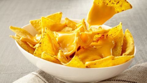 Käse schmelzt über knusprigen Tortilla-Chips in einer weißen Schüssel, während ein Chips auf das Käsedip zeigt.