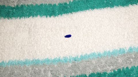 Auf einem gestreiften Handtuch liegt ein kleiner blauer Kugelschreiberfleck, der die Oberfläche verschmutzt.