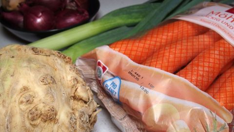 Frische Karotten, Lauch und Sellerie liegen neben roten Zwiebeln auf einer Oberfläche, bereit für den Einkauf im Supermarkt.