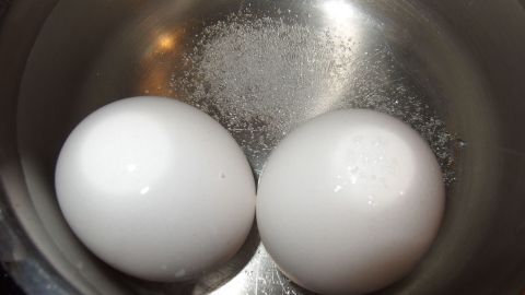 Zwei weiße Eier liegen in einem Topf mit Wasser, in dem Salz hinzugefügt wurde, um sie zu kochen.