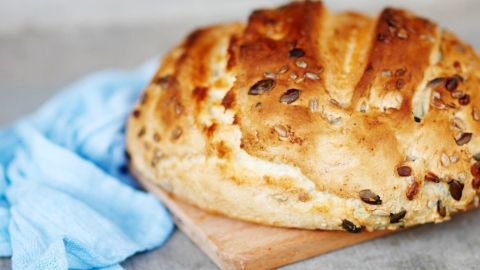 Ein frisch gebackenes Brot liegt auf einem Holzbrett, umgeben von einem blauen Tuch, bereit zum Servieren.