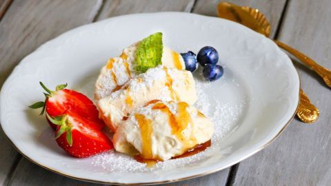 Eine cremige Joghurtmousse mit Honig liegt auf einem eleganten Teller, umgeben von frischen Beeren und Minze.