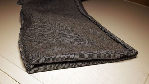 Jeans halten länger, wenn man sie beim Waschen auf links dreht und die Hosenbeine nach innen einschlägt. Helle Jeans liegen gefaltet auf einer Waschmaschine, bereit für die Wäsche, um ihre Lebensdauer zu verlängern.