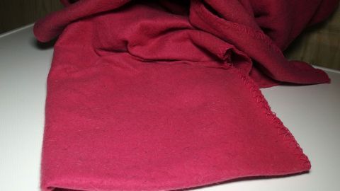 Fleece immer auf links waschen und nicht schleudern. Ein rotes Fleece liegt auf einem Tisch, bereit zum Waschen, um seine Farbe und Weichheit zu erhalten.