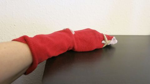 Alte Baumwollsocken eignen sich hervorragend, um damit Staub zu wischen. Die Socke einfach über die Hand stülpen und los geht's. Ein roter alter Baumwollsocken wird als improvisierter Reinigungshandschuh benutzt, um einen Tisch abzuwischen.