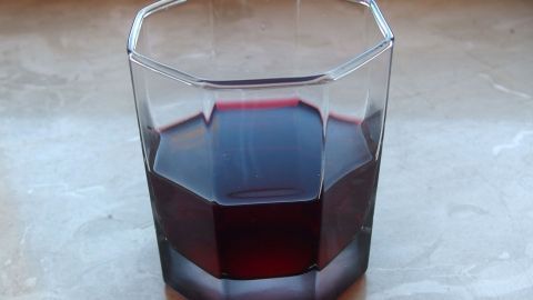 Ein Glas mit dunkelrotem Johannisbeersaft steht auf einer hellen Oberfläche und wartet darauf, getrunken zu werden.
