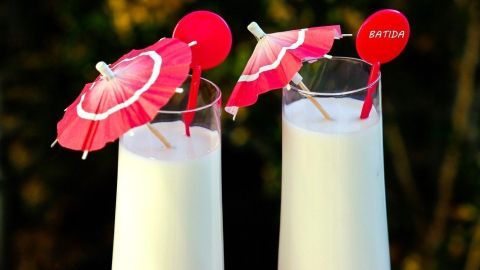 Milch mit Batida oder Malibu macht diesen exotischen Drink aus. Zwei elegante Gläser mit exotischer Milch, dekoriert mit kleinen Schirmchen, stehen auf einem Tisch im Freien.