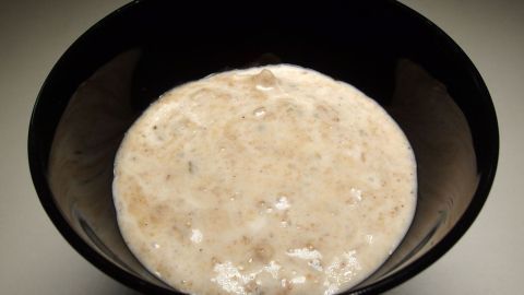 Eine cremige, beige Dessertmasse aus Spekulatiusresten liegt in einer schwarzen Schüssel auf einem neutralen Hintergrund.
