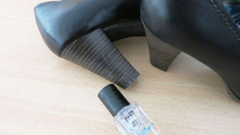 Schwarze Schuhabsätze stehen neben einer Flasche Klarlack auf einem hellen Tisch, bereit für die Pflege und den Schutz.