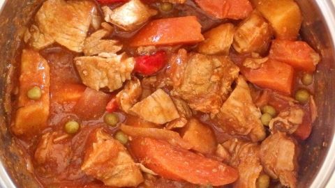 Wie man ein wunderbar zartes Gulasch mit Zwiebeln und Mehl zubereitet, verrät dir dieser Tipp. Ein zartes Gulasch mit Zwiebeln und buntem Gemüse kocht in einem Topf, umgeben von einer warmen Küche.