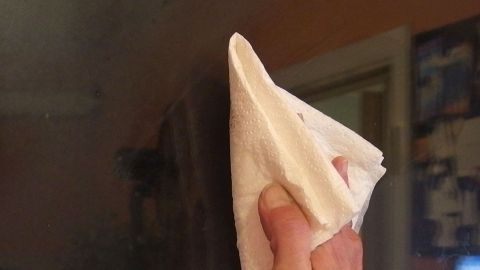 Mit kaltem Wasser und einem Schuss Essig glänzen die Scheiben besonders schön. Ein Handtuch reinigt ein Fenster, während kaltes Wasser für die Fenster im Hintergrund sichtbar bleibt.
