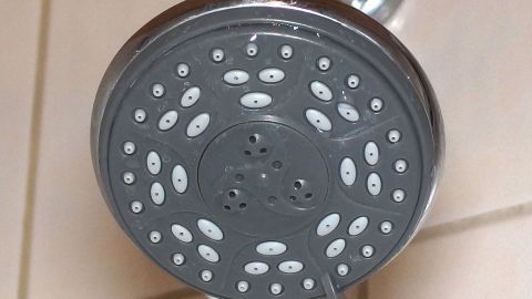 Verkalkte Brauseköpfe reinigen mit warmem Wasser und Haushaltsessig. Der verkalkte Brausekopf zeigt, wie Wasser durch die verstopften Düsen fließt, um in einem Badezimmer zu sprudeln.