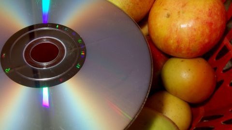 Eine glänzende CD-ROM liegt neben roten und grünen Äpfeln in einem Korb, was eine Fruchtfliegenfalle zeigt.