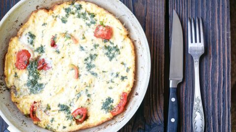 In einer Pfanne liegt ein Omelette mit Frischkäse und Cherrytomaten, umgeben von einem rustikalen Holzuntergrund.