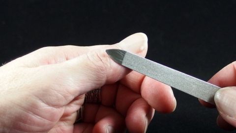 Eine Hand hält eine Nagelfeile, während sie vorsichtig versucht, Sekundenkleber von der Haut zu entfernen.