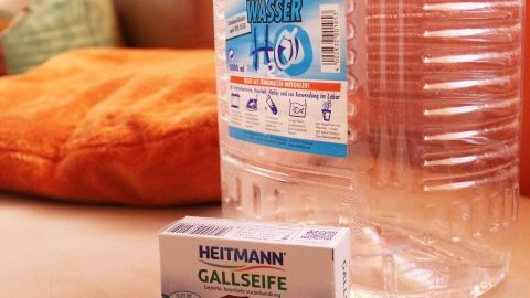 Ein Mikrofaserpolster steht neben einer Flasche mit destilliertem Wasser und einer Box Gallseife auf einem Tisch.