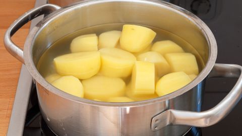 Kartoffelwasser ist nicht nur zum Kochen gut! Im Artikel erfährst du, wie du es clever nutzen kannst, um weiß lackierte Schränke und Türen wieder zum Strahlen zu bringen. Einfach und umweltfreundlich! Kartoffeln kochen im Metalltopf auf modernem Herd; gelbe Kartoffelstücke in Wasser umgeben von Holz- und Glaskeramik.
