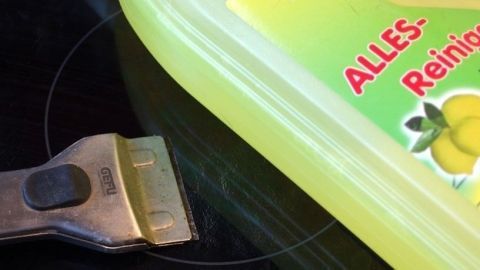 Ein Glaskeramikfeld wird mit einem Schaber gereinigt, während ein Allzweckreiniger daneben steht.