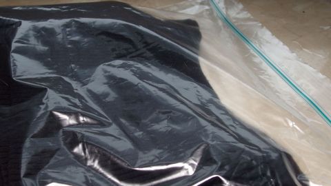 Ein schwarzes Kleidungsstück liegt in einem Ziploc-Beutel, der versiegelt ist, auf einer neutralen Oberfläche.