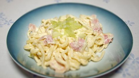 Gurkenspätzle liegen appetitlich auf einem blauen Teller, umgeben von einer gedeckten Tischoberfläche.