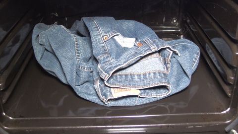Eine zerknitterte Jeans liegt im Backofen, während dieser möglicherweise zum schnellen Trocknen genutzt wird.