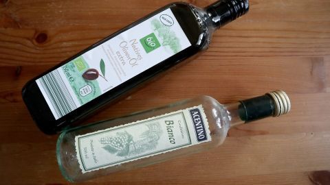 Zwei Flaschen stehen auf einem Holztisch: Eine dunkle Flasche mit Öl und eine klare mit Essig, bereit für die Möbelpolitur.