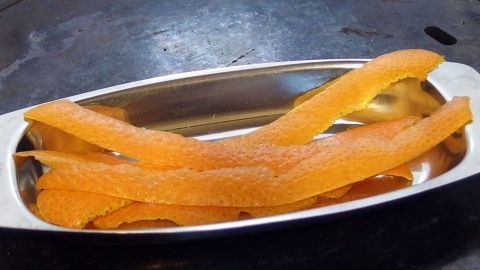 Orangene Schalen liegen in einer silbernen Schale, während sie eine fruchtige Zitonenschnitte für das Aroma freigeben.