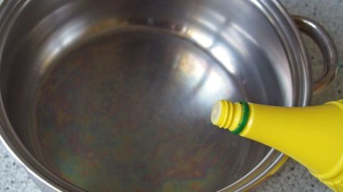 Regenbogenartig schimmernde Pfannen lassen sich mit Zitronensäure reinigen. Ein metallener Topf glänzt regenbogenartig, während eine Flasche Zitronensäure darüber geleert wird.