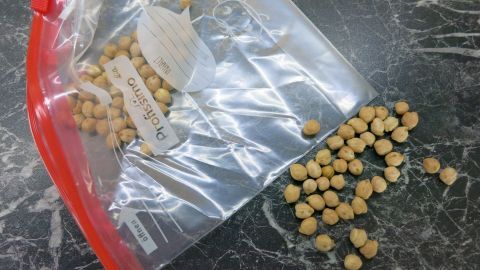 Selbst gemachtes Kühlpad mit Trockenerbsen: Die Herstellung ist simpel und geht schnell. Probier's aus. Ein Ziploc-Beutel mit Trockenerbsen liegt auf einer glänzenden Oberfläche, während einige Erbsen daneben verstreut sind.