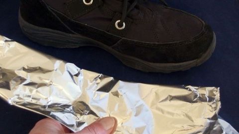 Ein Hand hält einen Streifen Aluminiumfolie, während ein schwarzer Schuh daneben liegt, um damit für Wärme zu sorgen.