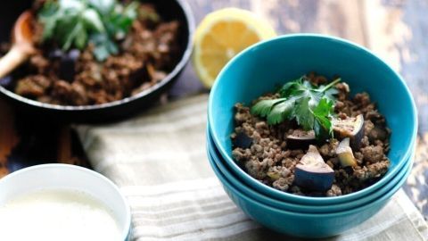 Eine bunte Auberginen-Hackfleisch-Pfanne wird in einer Schüssel serviert, umgeben von frischen Zutaten und einer Sauce.