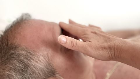 Ein Mann liegt im Bett und wird sanft am Gesicht berührt, um sein lästiges Schnarchen zu verhindern.