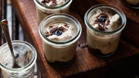 Vier Gläser mit Herrencreme stehen auf einem hölzernen Untergrund, dekoriert mit Schokoladenstückchen und einer ganzen Blaubeere.