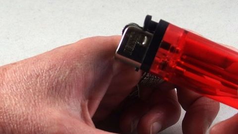 Eine Hand hält ein rotes Feuerzeug, das kurz davor ist, angezündet zu werden, um Hitze bei Insektenstichen zu erzeugen.