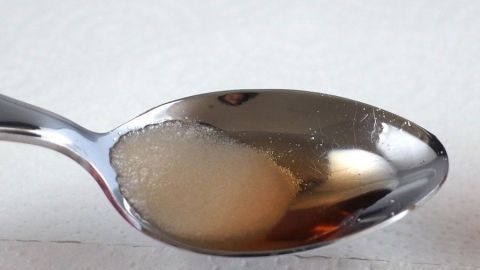 Zucker und Essig sollen effektiv gegen Schluckauf helfen. In diesem Bild siehst du einen Teelöffel mit einer Mischung aus beiden. Probiere diesen Tipp aus, um deinen Schluckauf schnell zu lindern. Ein glänzender Löffel mit Zucker und Essig steht bereit, um Schluckauf zu bekämpfen, auf einem weißen Untergrund.