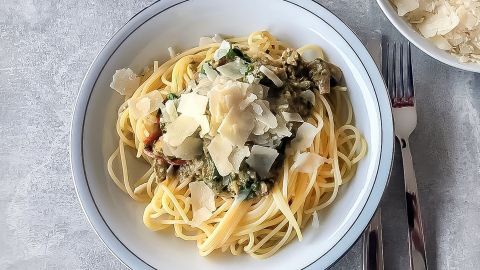 Eine Schüssel Spaghettisalat mit Parmesan ist ansprechend angerichtet und von frischen Zutaten umgeben, während ein Schälchen mit mehr Parmesan daneben steht.