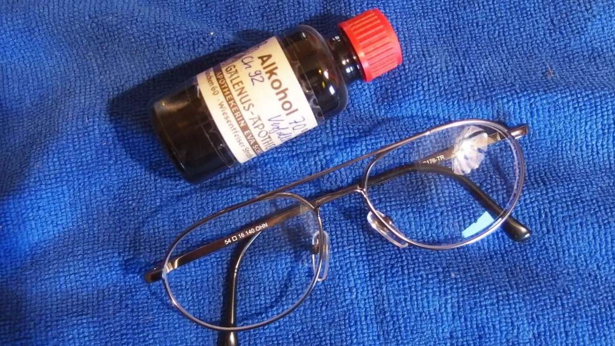 Eine Brille liegt auf einem blauen Tuch, neben ihr steht eine Flasche Alkohol, bereit zum Putzen der Gl&auml;ser.