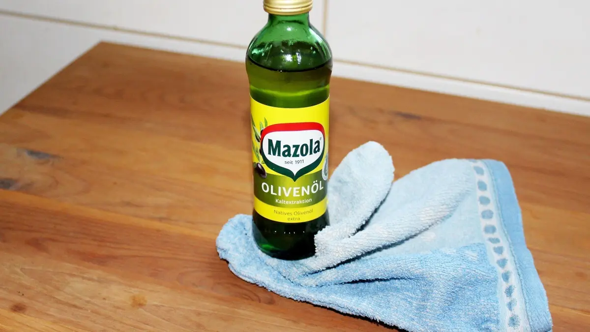Ein Flasche Oliven&ouml;l steht auf einem Holzoberfl&auml;che, umgeben von einem blauen Tuch, bereit zur Behandlung von Kiefernm&ouml;beln.